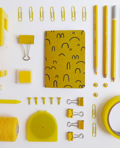 Gold patterned notebook on a desk with yellow office supplies