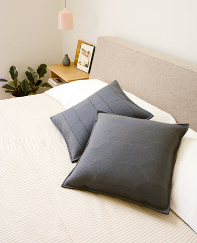 Two grey wool felt throw pillows on a bed