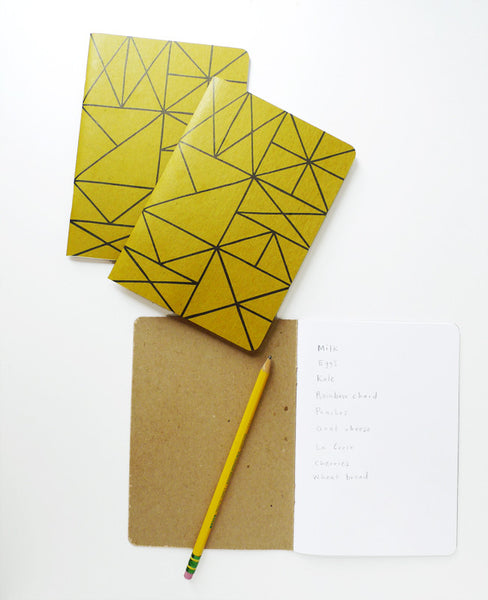 Three gold grid notebooks - one open with a pencil