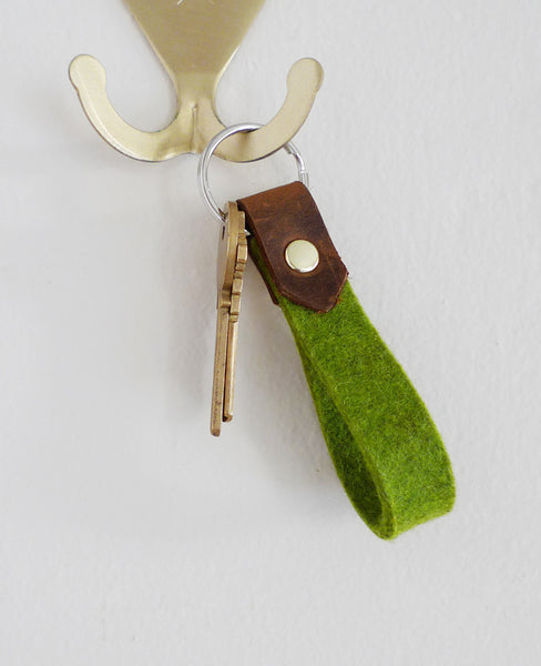 Green keychain from Cotton & Flax hanging from a brass hook