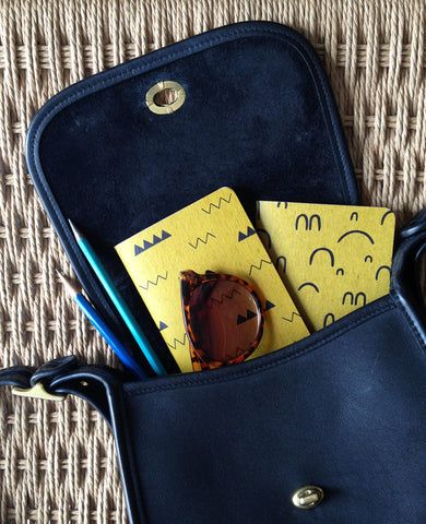 Two gold patterned pocket notebooks inside a black purse